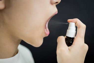 Ağızına ilaç sıkan Asyalı bayan, ağızında dezenfekte, solunum yolu enfeksiyonunun önlenmesi veya Coronavirus COVID-19, mikrop akciğerlere girmeden önce boğazdaki bakteriye karşı koruma sağlar.