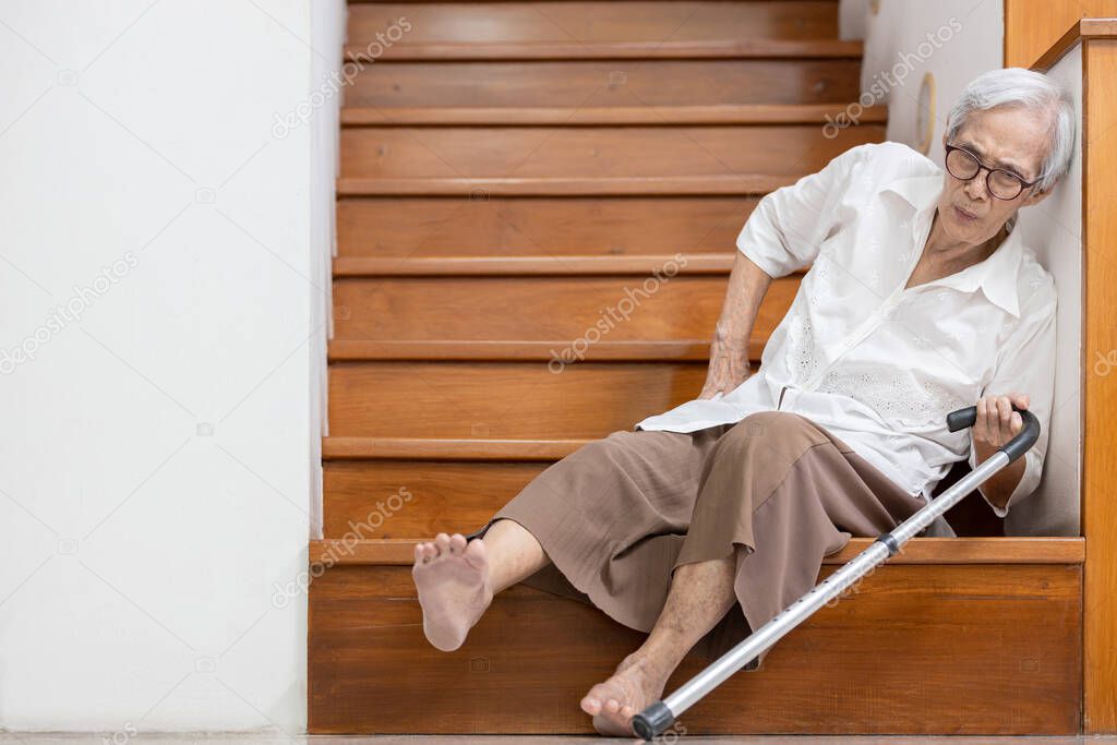 Senior woman sitting on the floor of the staircase with pain in hips and back,tripped or lose balance as she walked downstairs causing accidents,old elderly slipped and fell was injured by dizziness