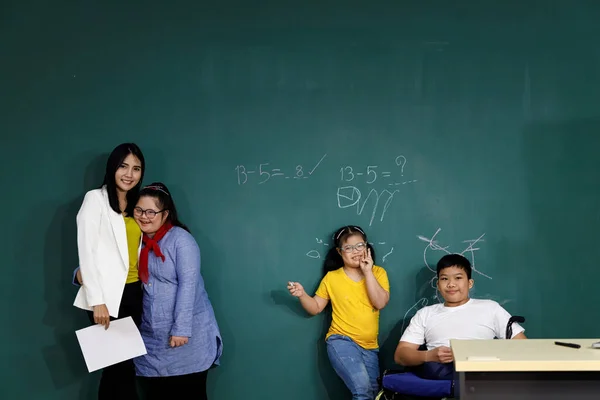 Teacher with Asian girls with Down\'s syndrome and disabled boy on wheelchair in classroom.