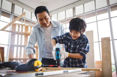 Baba oğluna marangozluk atölyesinde elektrikli matkap kullanmayı öğretiyor. Aile kavramı evde birlikte hobi yapıyor..