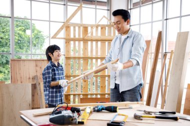 Asyalı oğul marangozluk atölyesinde babasına kereste uzatıyor. Baba oğul birlikte ahşap işi yapıyor..