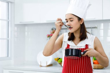 Kırmızı önlüklü Asyalı kadın şef esrardan çorba tadında. Kavramsal kadın evde yemek hazırlıyor..