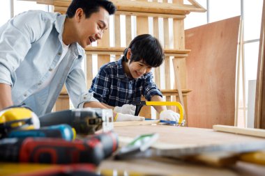 Baba oğluna marangozluk atölyesinde testere kullanmayı öğretiyor. Aile kavramı evde birlikte hobi yapıyor..