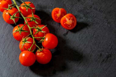 Güzel, taze, sarmaşık domatesleri (kiraz), bir damla su, çiğ, bütün ve yarım. Siyah desenli arka planda. Akdeniz diyetinin içeriği. Kopyalama alanı olan üst görünüm.
