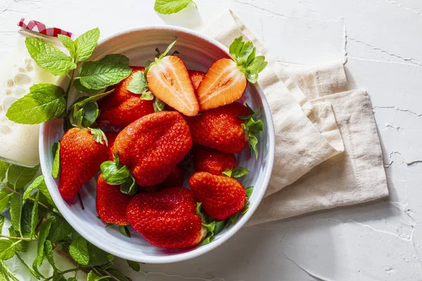 Lezzetli büyük çilekli kase (fresones), taze, taze kesilmiş, sütlü ve naneli. Hassas beyaz dokulu arka planda. Kopyalama alanı olan üst görünüm.