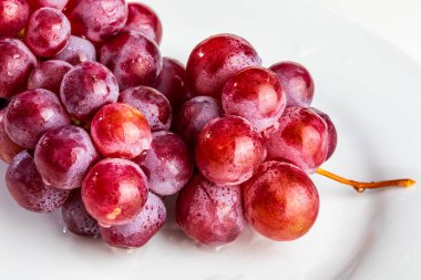Masanın üzerinde güzel bir kırmızı üzüm kümesi (mürekkep) var. Taze, çiğ ve su damlaları.