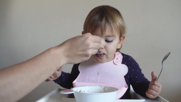 家庭でスプーンとスプーンと母親の給餌子.空腹の子供とともにシリコーンビブ — ストック動画