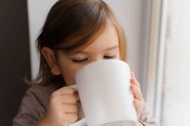 Çocuk büyük beyaz kupanın penceresinin yanında kakao ya da süt içer. kupa maketi. Noel zamanı.