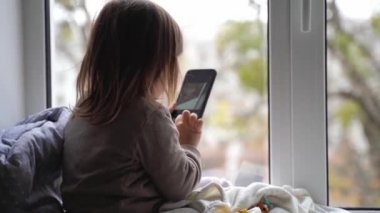 Küçük çocuk evde telefon kullanıyor, fotoğraf çekiyor ve oyun oynuyor.