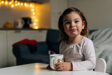 Kafkasyalı küçük kız evdeki bardaktan kakao içiyor. Noel ışıkları