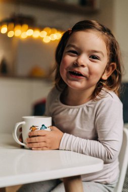 Kafkasyalı küçük kız evdeki bardaktan kakao içiyor. Noel ışıkları