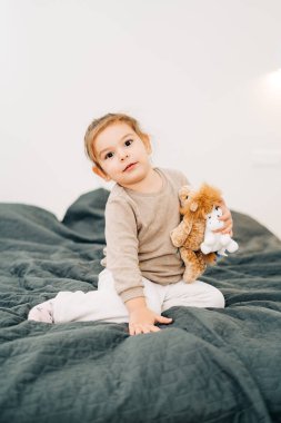 Küçük güzel kız, uzun boylu, yatakta oturuyor.