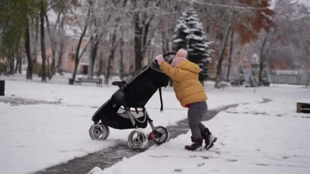 Küçük çocuk, içinde kardeşi olan bir bebek arabasını itiyor. Kış karlı bir gün. Noel zamanı — Stok video