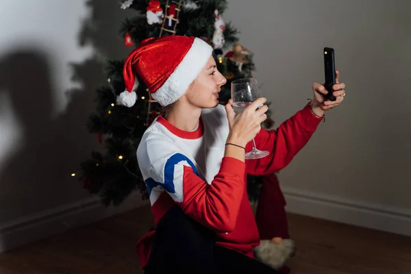 圣诞节前夕，千禧年的年轻女子在家里用电话。网上购物、检疫虚拟庆祝 — 图库照片