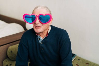 Evde kalp şeklinde gözlüklerle mutlu yaşlı adam portresi, aşk konsepti.