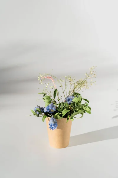 Ramo de flores secas en taza de papel artesanal sobre fondo blanco con luz solar y sombras —  Fotos de Stock