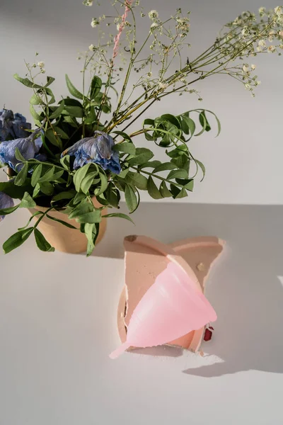 Copa menstrual rosa con flores sobre fondo blanco con luz solar y sombras —  Fotos de Stock