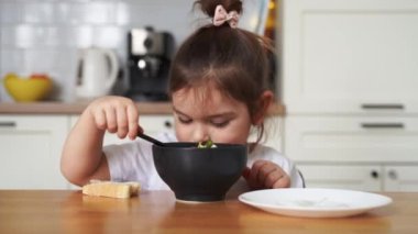 Evdeki mutfakta yemek seçen küçük kız. Kaşıkla yemek yemeyi öğrenmek. Çocukların kötü sofra adabı.