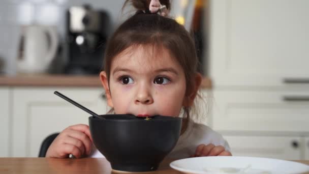 蹒跚学步的小女孩在家里厨房里挑食。学着用勺子吃饭。小孩子的餐桌礼仪不好 — 图库视频影像