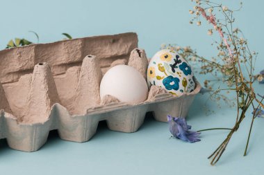 Çiçek desenli boyanmış tavuk yumurtası. Paskalya tatili için çocuklarla el işi. Botanik dekorasyonu. Mavi arka planda minimum paskalya yumurtası. Bahar tatili için el işi