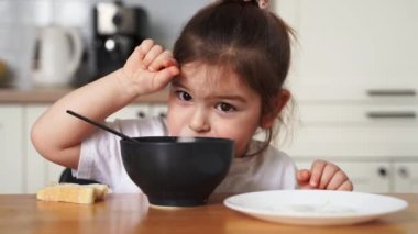 Evdeki mutfakta yemek seçen küçük kız. Kaşıkla yemek yemeyi öğrenmek. Çocukların kötü sofra adabı.