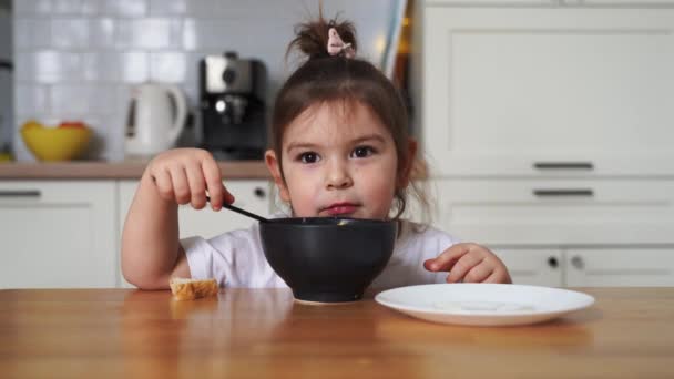 Tout-petit fille mangeur difficile à la maison cuisine. apprendre o manger avec une cuillère. mauvaises manières de table de l'enfant — Video