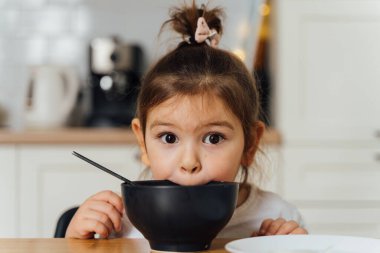 Evdeki mutfakta yemek seçen küçük kız. Kaşıkla yemek yemeyi öğrenmek. Çocukların kötü sofra adabı.