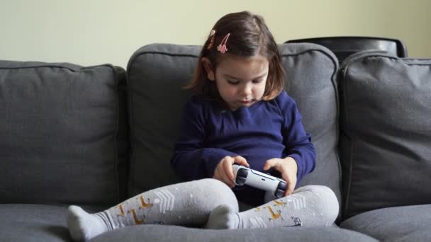 Menina criança jogando console de videogame em casa na sala de estar no sofá. Jovem garoto gamer. — Vídeo de Stock