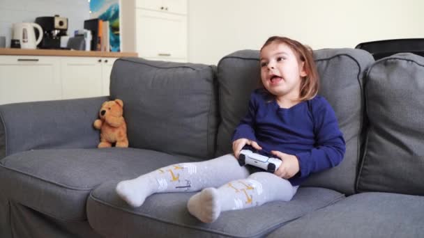Тоддлер девушка играет в видео игры консоли дома в гостиной на диване. Молодой геймер. — стоковое видео