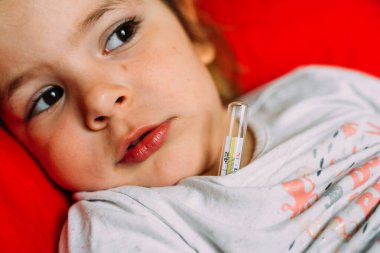 Civa termometresi olan küçük kız evde yatıyor. Çocuğun vücut ısısı yüksek. Hasta, daha az, enfeksiyon.