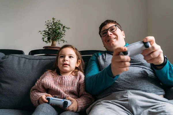 Happy Caucasian father and little 3s daughter sit on couch at home have fun playing computer video game together. Overjoyed dad and small girl child enjoy family weekend engaged in funny activity. — Stock Photo, Image