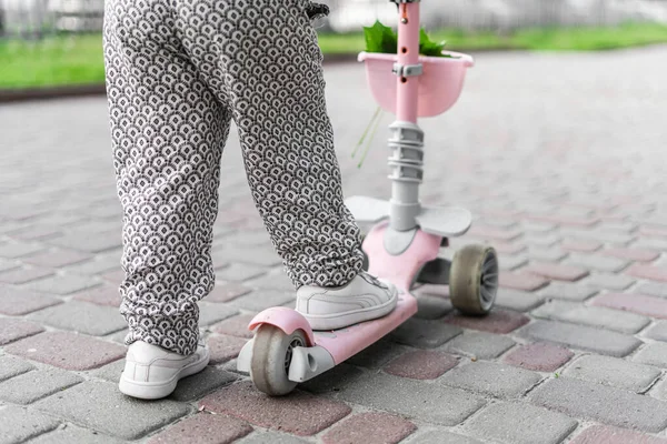 Pattes d'enfant sur mini scooter rose dans la ville européenne. Activités estivales en plein air pour les enfants. Les tout-petits jouent dans les zones urbaines. Parentalité durable — Photo