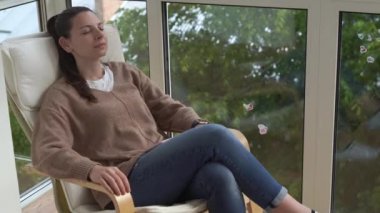 Evdeki balkonda oturan bir kadın koltukta oturuyor ve uyuyor. Meditasyon, rahatlama, dışavurum