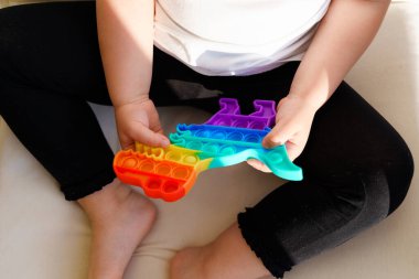 Gökkuşağı renginde popit oyuncağı olan küçük bir kız. Stres atmak için dino şeklinde silikon oyuncak. Kabarcıklar duyusal modayı takip ediyor. Çocuk evde samimi bir şekilde oynuyor