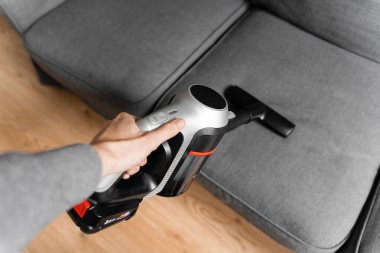 Kablosuz elektrik süpürgesiyle gri kanepeyi temizliyorum. El bilgisayarı kablosuz temizleyici. Ev aletleri. Ev işi modern ekipmanlar