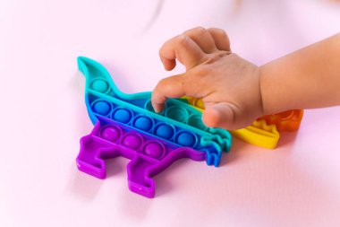 Gökkuşağı renginde ve dino şeklinde Popit gökkuşağı oyuncağı. Moda baloncuklu pop müziği. Stres önleyici tuhaf bir eğilim. pembe arkaplan ve parmak kabarcıkları patlatıyor.