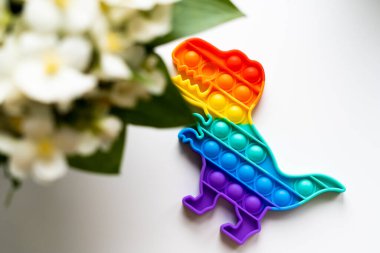 Gökkuşağı renginde ve dino şeklinde Popit gökkuşağı oyuncağı. Moda baloncuklu pop müziği. Stres önleyici tuhaf bir eğilim. Beyaz arkaplan ve parmak kabarcıkları patlatıyor.