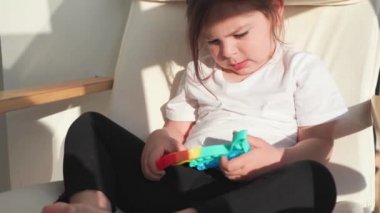 Gökkuşağı renginde popit oyuncağı olan küçük bir kız. Stres atmak için dino şeklinde silikon oyuncak. Kabarcıklar duyusal modayı takip ediyor. Çocuk evde samimi bir şekilde oynuyor