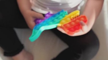 Gökkuşağı renginde popit oyuncağı olan küçük bir kız. Stres atmak için dino şeklinde silikon oyuncak. Kabarcıklar duyusal modayı takip ediyor. Çocuk evde samimi bir şekilde oynuyor