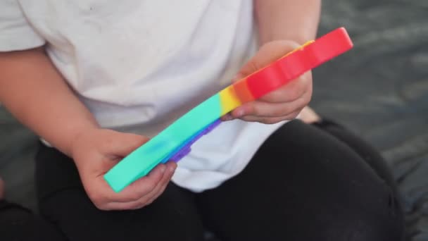 Peuter meisje met popit speelgoed in regenboogkleuren. Dino vorm siliconen speeltje voor stress verlichting. Bubbles zintuiglijke trendy fidget. Kind speelt thuis in openhartige stijl — Stockvideo