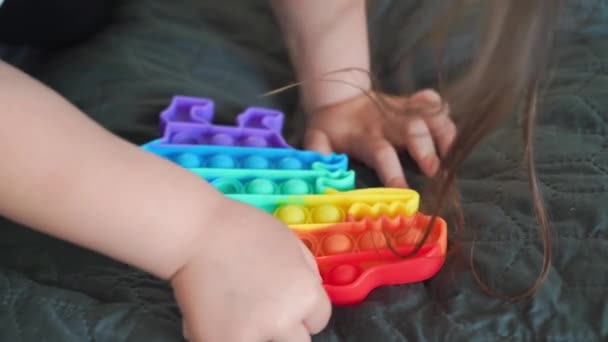 Niña pequeña con popit toy en colores arcoíris. Dino forma de juguete de silicona para aliviar el estrés. Burbujas sensorial moda nerviosa. Niño jugando en casa en estilo franco — Vídeos de Stock