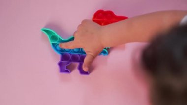 Gökkuşağı renginde ve dino şeklinde Popit gökkuşağı oyuncağı. Moda baloncuklu pop müziği. Stres önleyici tuhaf bir eğilim. pembe arkaplan ve parmak kabarcıkları patlatıyor.