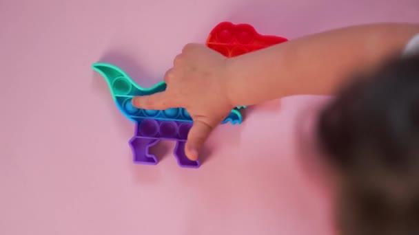 Popit brinquedo arco-íris em cores do arco-íris e forma de dino. Fidget pop bolha na moda. Tendência sensorial anti stress engraçado. fundo rosa e dedo estalando as bolhas. — Vídeo de Stock