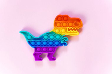 Gökkuşağı renginde ve dino şeklinde Popit gökkuşağı oyuncağı. Moda baloncuklu pop müziği. Stres önleyici tuhaf bir eğilim. pembe arkaplan ve parmak kabarcıkları patlatıyor.