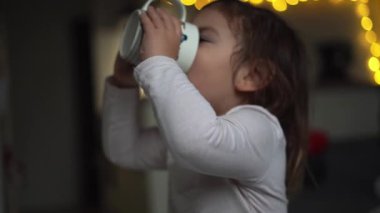 Kafkasyalı küçük kız evdeki bardaktan kakao içiyor. Noel ışıkları