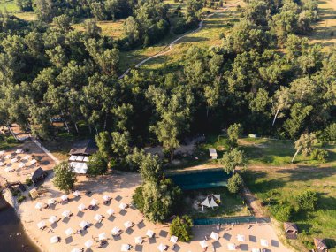 Nehir kumsalının yukarıdan görünüşü, dinlenme yerleri ve şemsiyeler. Yerel seyahat konsepti. Sürdürülebilir yaşam tarzı, karbon ayak izini azaltıyor. Nehir kenarındaki tatil beldesinin insansız hava aracı görüntüsü