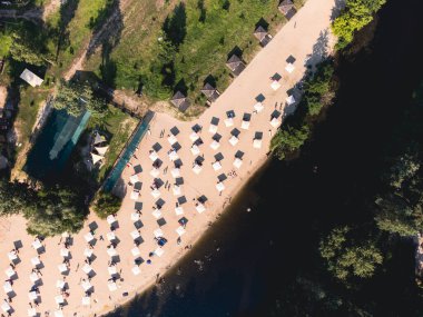 Nehir kumsalının yukarıdan görünüşü, dinlenme yerleri ve şemsiyeler. Yerel seyahat konsepti. Sürdürülebilir yaşam tarzı, karbon ayak izini azaltıyor. Nehir kenarındaki tatil beldesinin insansız hava aracı görüntüsü