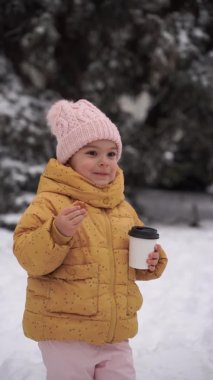 Kışın karlı bir günde kakao içen ve dışarıda kurabiye yiyen bir kız çocuğu. Mutlu çocukluk aktiviteleri. Noel tatili. Soğuk hava