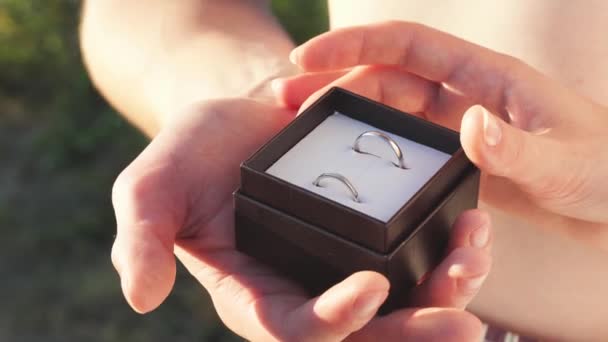 Cierre de la caja del anillo con un par de manos al aire libre. Soleado atardecer día de verano con los amantes y propuesta de matrimonio. — Vídeo de stock