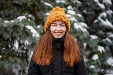 Ormanda gülümseyen bir kadın. Kameraya bakan kızıl saçlı, gülümseyen bin yıllık bir kızın yaşam tarzı portresi. Karlı Noel Günü konsepti